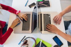 Métiers du numérique formation en alternance - Blog - Vue de dessus des mains du jeune homme et femme travaillant à l'ordinateur portable dans le bureau de travail collaboratif, en tapant sur le clavier